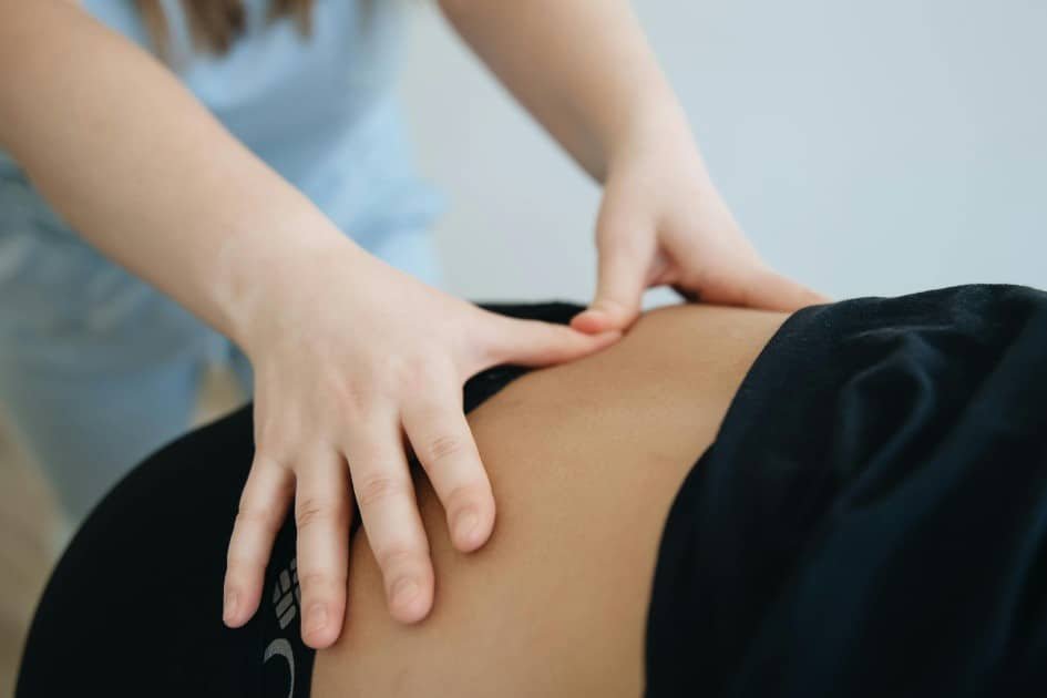 Fingers applying pressure to an acupressure point on the lower back to relieve pain.