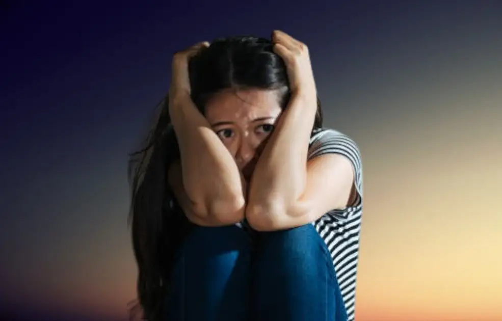 A person sitting alone in shadow, holding head down, surrounded by swirling thoughts.