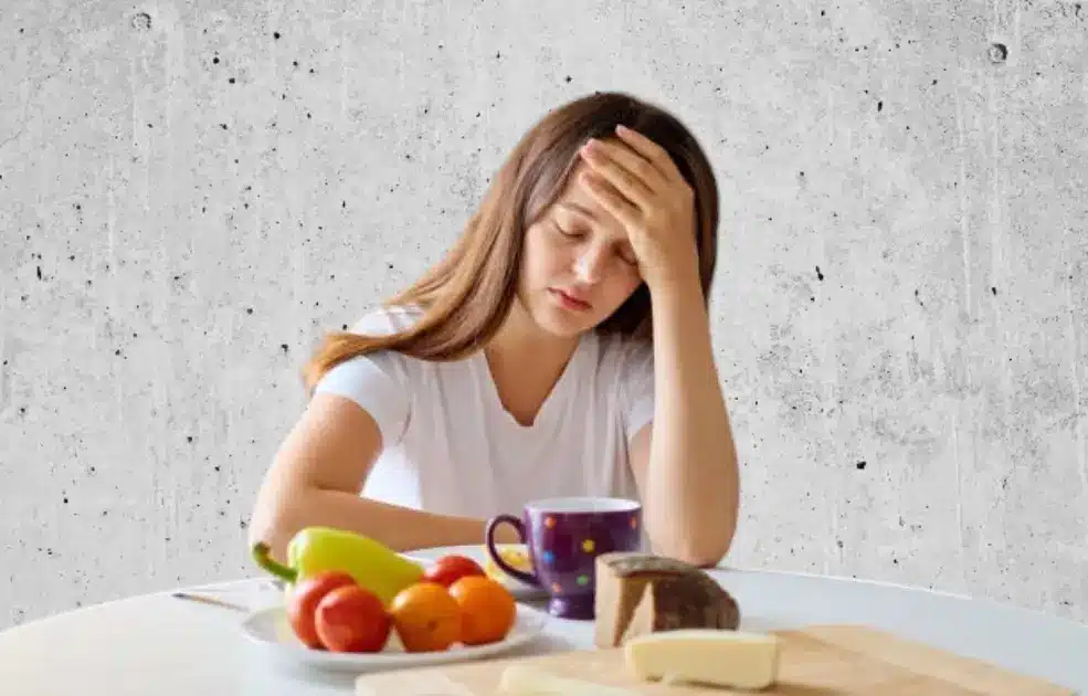 An anxious person sits at a table with untouched food, symbolizing the link between anxiety and poor eating habits.