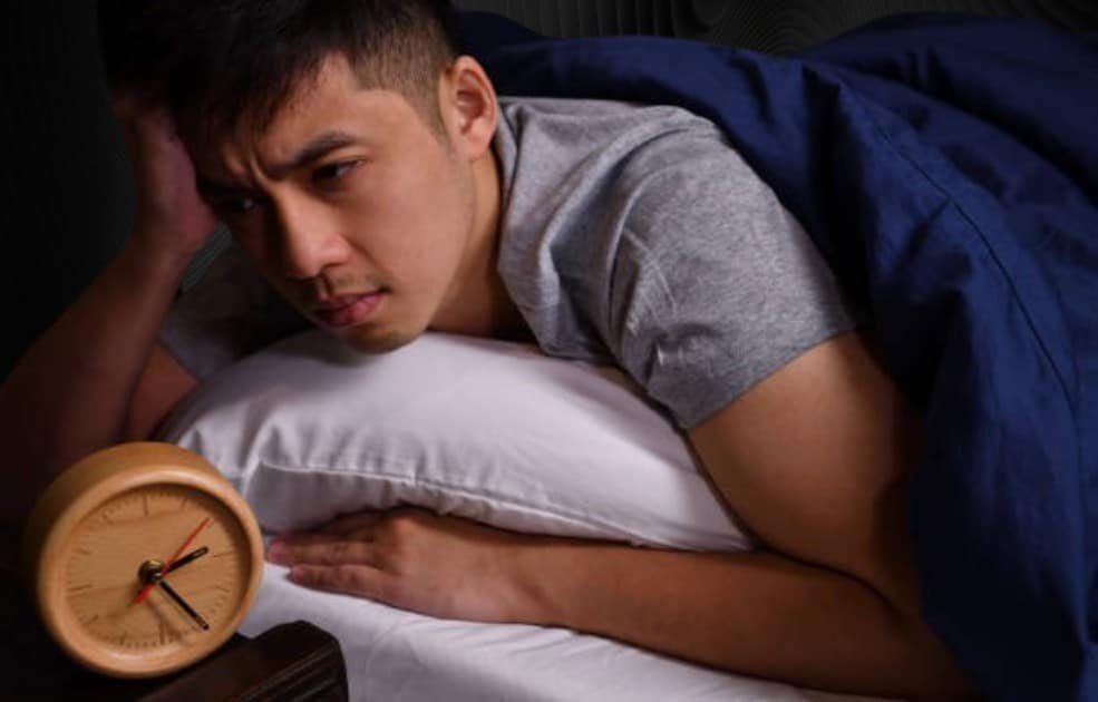 Person lying awake in bed, eyes wide open, surrounded by glowing devices, symbolizing anxiety and poor sleep habits.