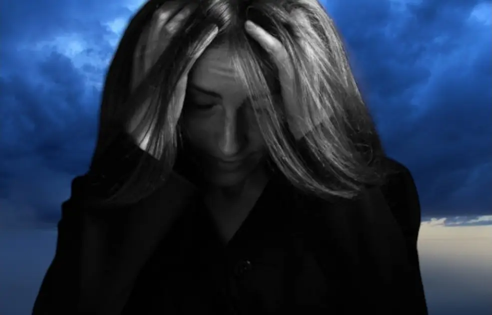 solitary figure sits in a dark room with their head in their hands, surrounded by a chaotic swirl of abstract shapes symbolizing overwhelming thoughts and chronic stress.