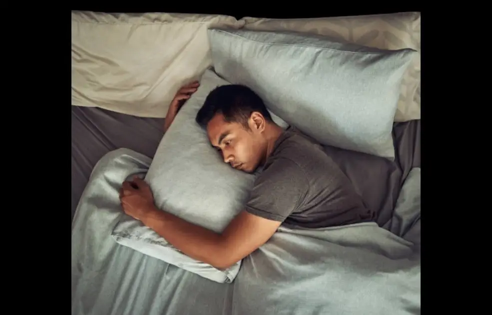 A person lying awake in bed at night, surrounded by darkness and clutter, eyes open with a distressed expression.