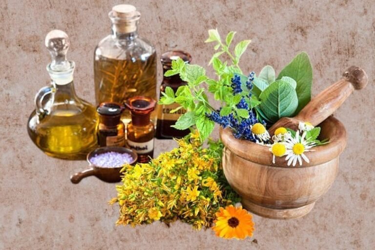 Bottles of essential oils surrounded by fresh herbs and flowers on a wooden surface.