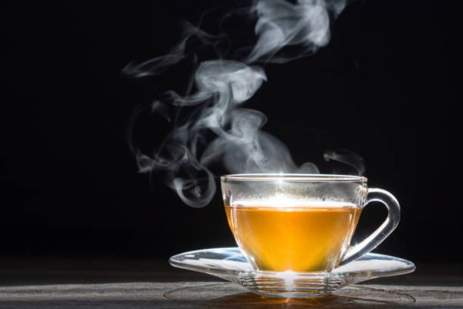 A steaming cup of green tea with fresh tea leaves and lemon on a wooden table, symbolizing immune-boosting benefits.