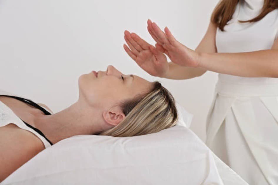 Hands channeling glowing energy over a relaxed body during a healing session.