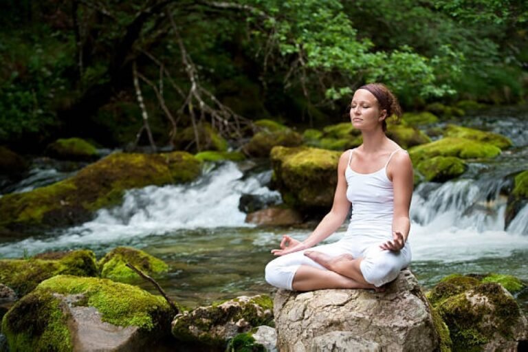 Woman meditating outdoors surrounded by natural elements representing holistic wellness.