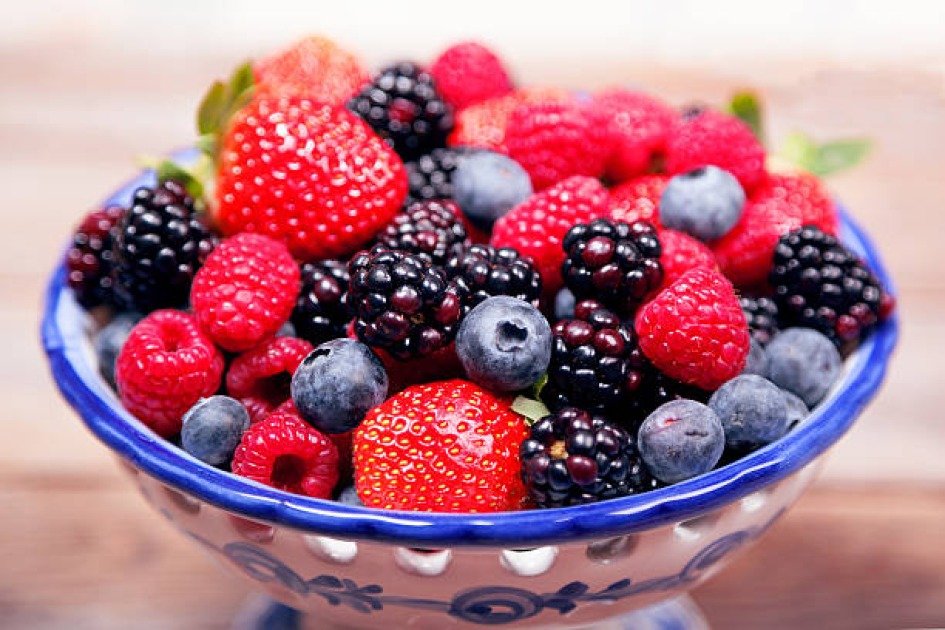 A vibrant assortment of fresh berries in a bowl with a clock in the background, symbolizing the balance of intermittent fasting.