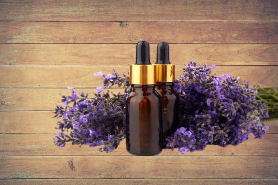 Close-up of a lavender oil bottle surrounded by fresh lavender flowers on a wooden table.