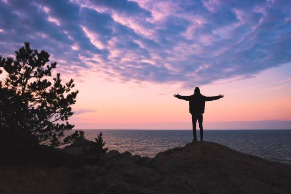 A person standing on a cliff at sunrise, releasing a handful of paper cranes into the sky, symbolizing freedom from anxiety and worry