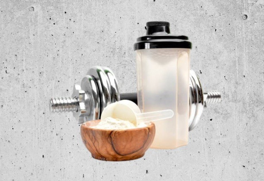 Scoop of protein powder beside a shaker bottle on a gym bench.