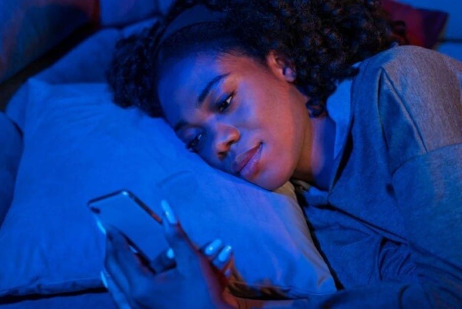 Stressed woman using phone in bed under blue light