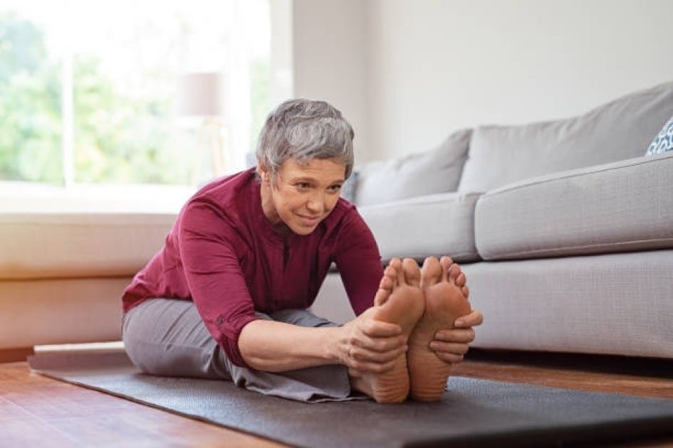 Senior woman stretching on yoga mat, focusing on recovery and sleep for fitness.