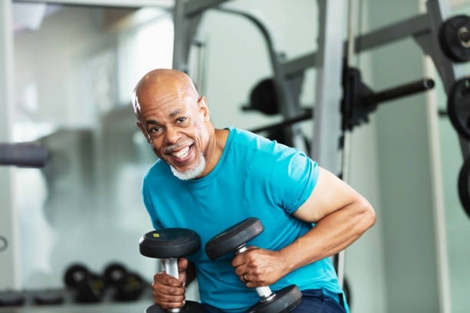 Active senior lifting dumbbells with confidence in a bright gym setting.