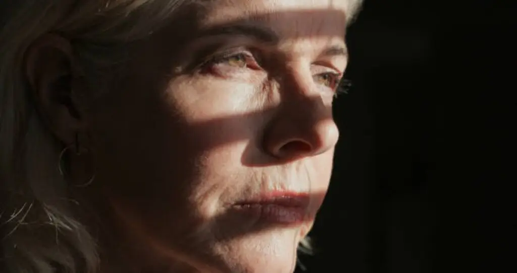 Tired woman under harsh lighting with wrinkles and fatigue visible, symbolizing accelerated aging from sleep deprivation.