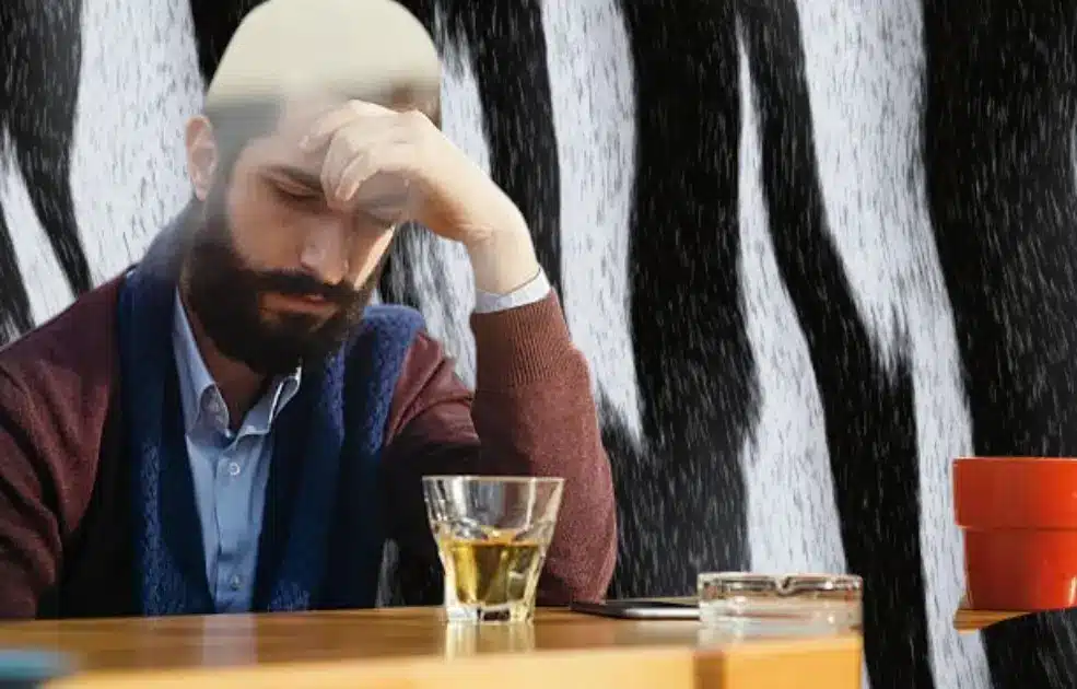 Person sitting alone in darkness with alcohol and pills nearby, symbolizing depression and substance abuse.