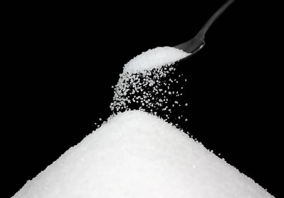 Overflowing spoonfuls of white sugar against a dark background symbolizing hidden health dangers.