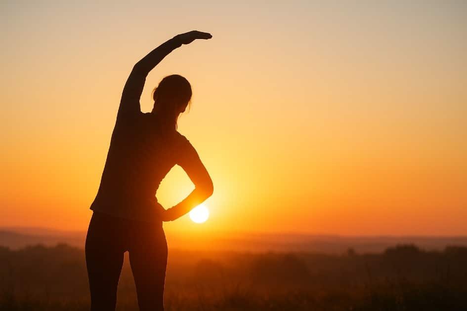 Woman stretching outdoors at sunrise emphasizing ideal workout timing for peak health